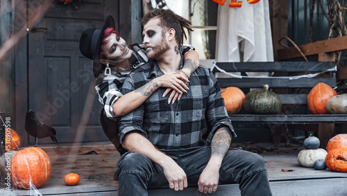 Scary love family couple man,woman celebrating halloween.Terrifying black skull half-face makeup,witch costumes.Stylish images,hat.Photoshoot,holiday party. Decorating of porch,pumpkin jack-o-lantern