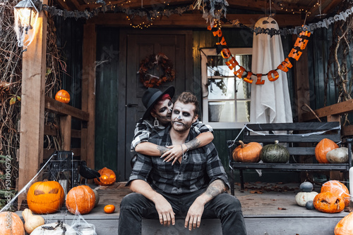 Scary love family couple man,woman celebrating halloween.Terrifying black skull half-face makeup,witch costumes.Stylish images,hat.Photoshoot,holiday party. Decorating of porch,pumpkin jack-o-lantern