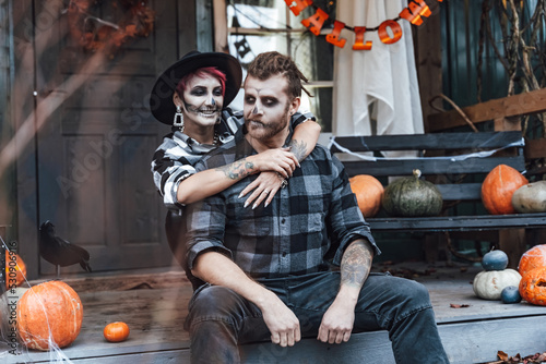 Scary love family couple man,woman celebrating halloween.Terrifying black skull half-face makeup,witch costumes.Stylish images,hat.Photoshoot,holiday party. Decorating of porch,pumpkin jack-o-lantern