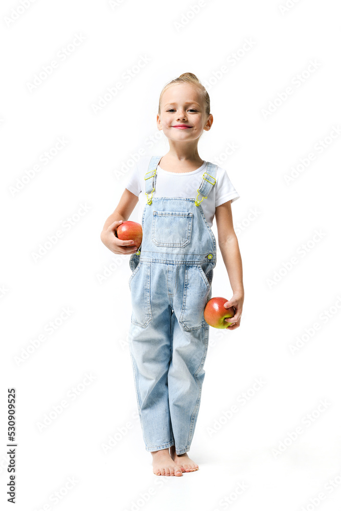 Cute girl dressed in denim overalls with apples on a white background. Cute girl dressed in denim overalls with apples on a white background.