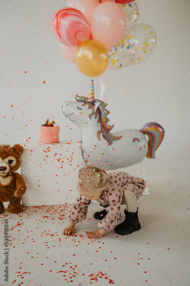 Fototapeta premium Little girl on the background of balloons, cake and confetti. Little girl's birthday.