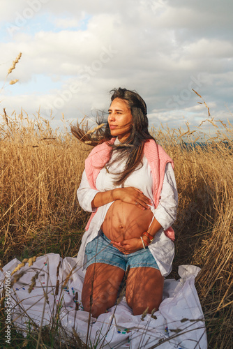 Young pregnant latin woman seated on a wheat field