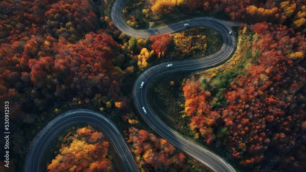 aerial footage of curved road on autumn, beautiful curved pass with vehicles and colorful autumn nature colors on trees with sunset light