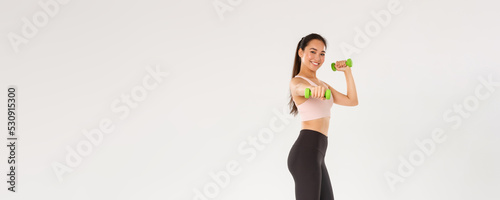 Sport, gym and healthy body concept. Full length of smiling active and healthy girl athlete, sportswoman in sportswear, extending hand with dummbells, workout in gym, doing fitness exercises photo