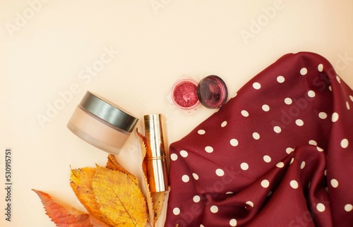 Autumn, fashion concept. Polka dot scarf, cosmetics and yellow autumn leaves on a beige background. Copy space, top view, background, postcard.