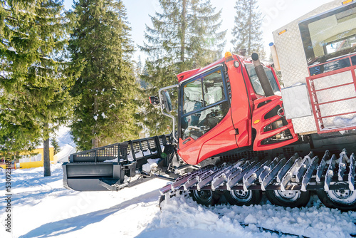 Red modern snowcat ratrack with snowplow,snow grooming machine,remover truck preparing ski slope,piste,hill at alpine skiing winter resort. Heavy machinery,tractor mountain equipment track vehicle