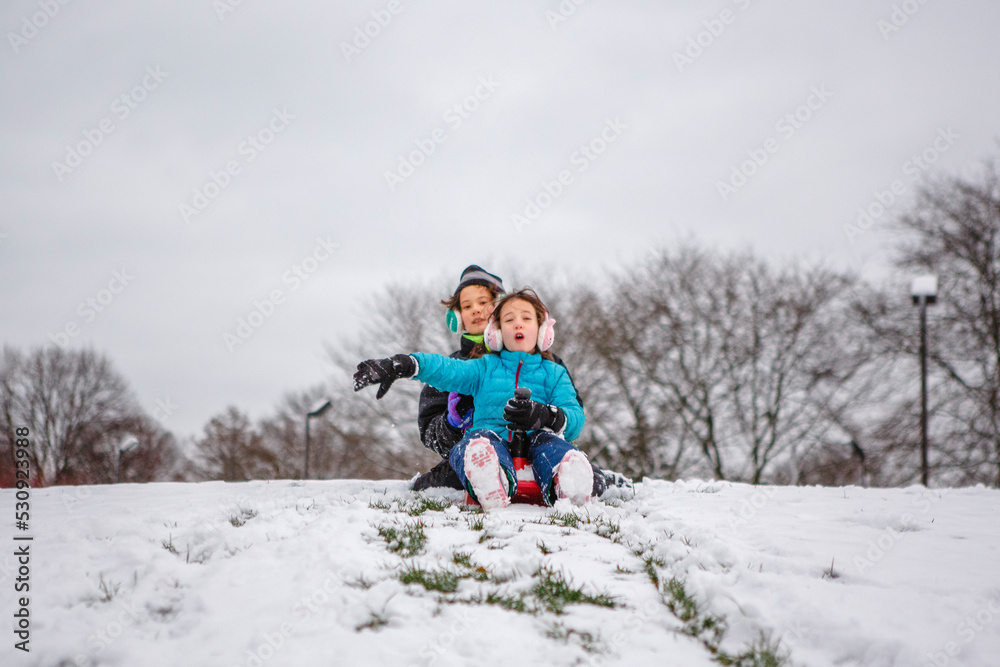 Two children slide down a snowy hill together in winter Two children slide down a snowy hill together in winter