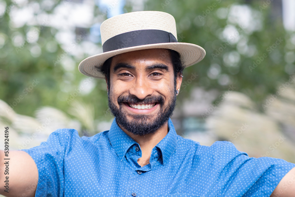 young man with beard and summer hat outside laughing