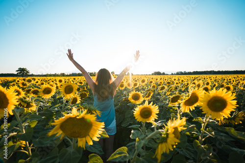 Woman standing in middle of sunflower field full of blooms at sunset.