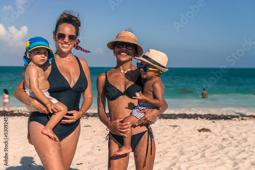 Two latin moms carrying her babies at the beach on a sunny day