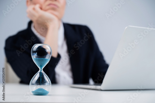 Business woman is bored at work and looks at the hourglass.