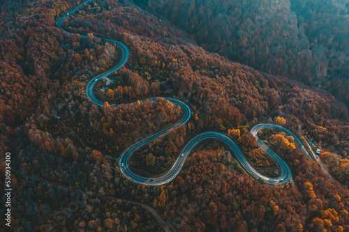 aerial photography of curved road on autumn, beautiful curved pass with vehicles and colorful autumn nature colors on trees with sunset light