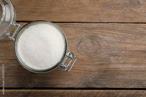 Granulated sugar in glass jar on wooden table, top view. Space for text