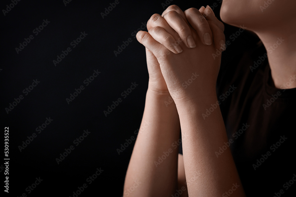 Fototapeta premium Woman holding hands clasped while praying against black background, closeup. Space for text