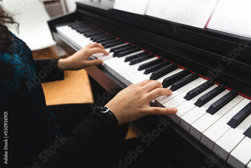 Side view of woman's hands playing piano by reading sheet music. Selective focus
