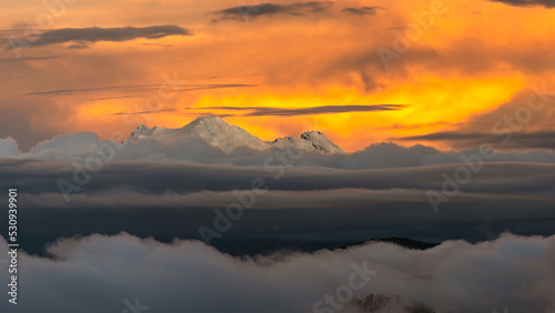 Panoramic view of the Antisana volcano illuminated by a gorgeous sunset light seen from west part of Quito and a bank of clouds and mist covers the valley and the city