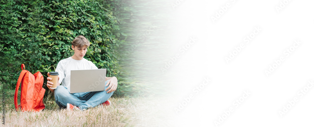 young man with laptop on his lap sits cross-legged against a green plant background. copy space young man with laptop on his lap sits cross-legged against a green plant background. copy space
