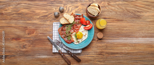 Plate with tasty fried egg, bacon and bread on wooden background, top view