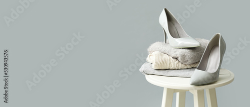 Table with stack of stylish sweaters and woman's shoes on grey background with space for text