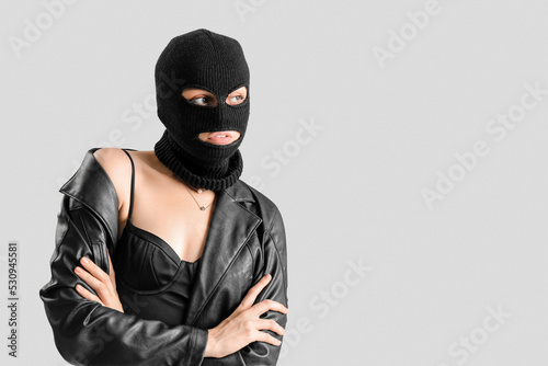 Young woman in balaclava and leather jacket with crossed hands on light background