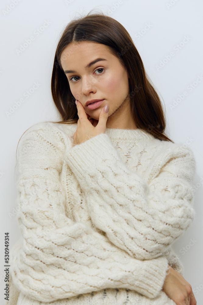 a beautiful, pleasant young woman stands on a light background in a stylish, warm autumn white sweater and poses with her arms crossed on her chest in a relaxed pose, looking sweetly at the camera a beautiful, pleasant young woman stands on a light background in a stylish, warm autumn white sweater and poses with her arms crossed on her chest in a relaxed pose, looking sweetly at the camera