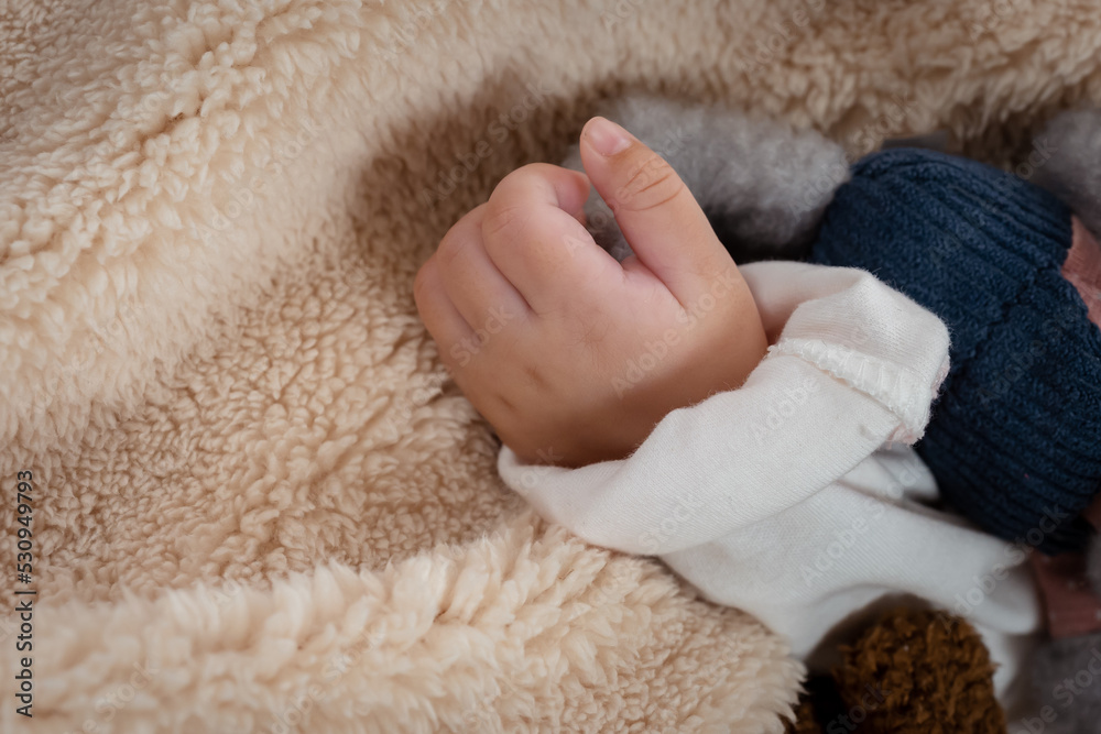 close-up of small hands of a 3-month-old Asian newborn with her left hand attached to the body of a little girl lying on a soft bed in the bedroom looking relaxed. close-up of small hands of a 3-month-old Asian newborn with her left hand attached to the body of a little girl lying on a soft bed in the bedroom looking relaxed.