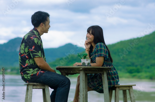Asian couple are sitting on chair with table on mountain and river background with smile face © bellito10