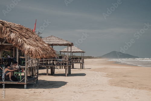 Danang, Vietnam - March 7th, 2020 : beach near Danang city on a sunny day with wooden huts on the side and mountains in the background