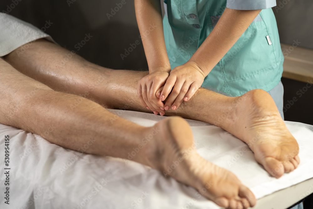 Foot massage. Physiotherapist massaging legs of young male athelete in spa