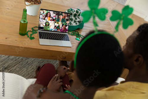 African american couple making st patrick's day video call to friends on laptop at home