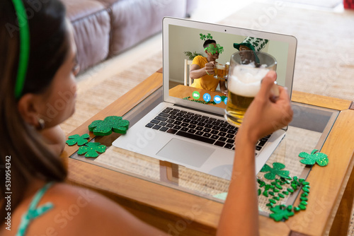 Caucasian woman holding beer while having a video call on laptop at home