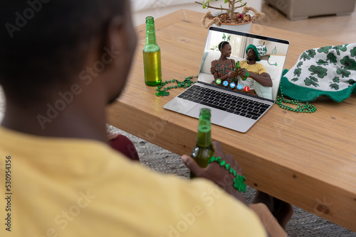 African american man holding beer while having a video call on laptop at home
