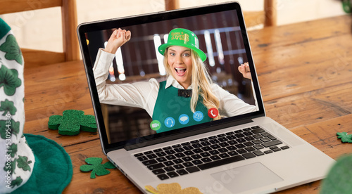 Webcam view of caucasian woman wearing green hat dancing on video call on laptop on wooden table