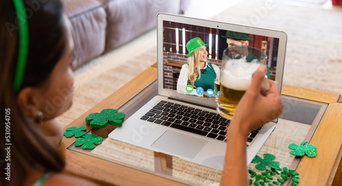 Caucasian woman holding a beer glass having a video call on laptop at home