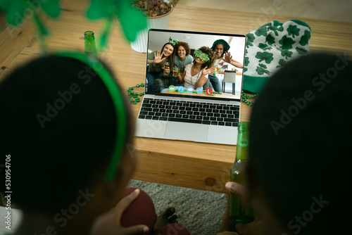African american couple making st patrick's day video call to waving friends on laptop at home