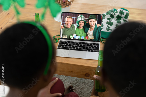 African american couple making st patrick's day video call to smiling male friends on laptop at home
