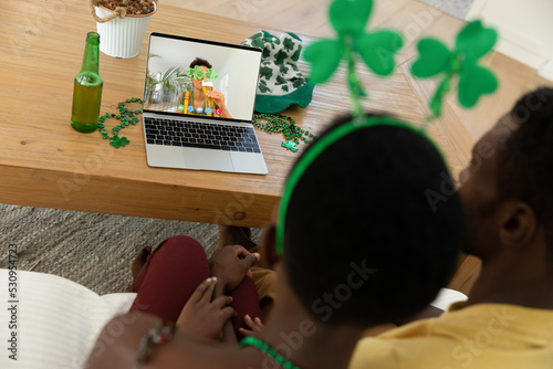 African american couple making st patrick's day video call to friend in costume on laptop at home