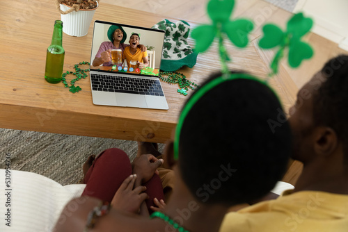 African american couple making st patrick's day video call to two male friends on laptop at home