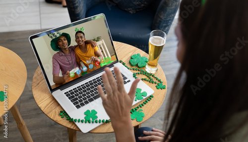 Caucasian woman with beer at bar making st patrick's day video call waving to friends on laptop