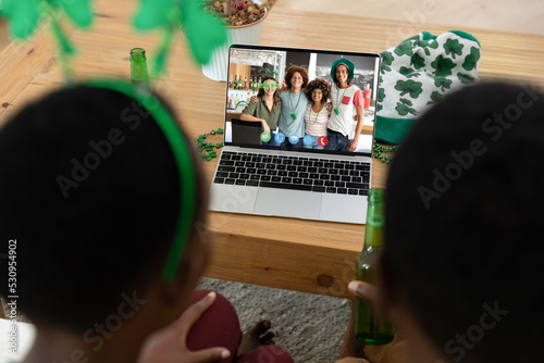 African american couple having st patrick's day video call with a group of friends on laptop at home