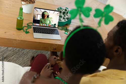 African american couple having st patrick's day video call with female friend on laptop at home