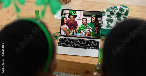 African american couple making st patrick's day video call with friends in costume on laptop at home