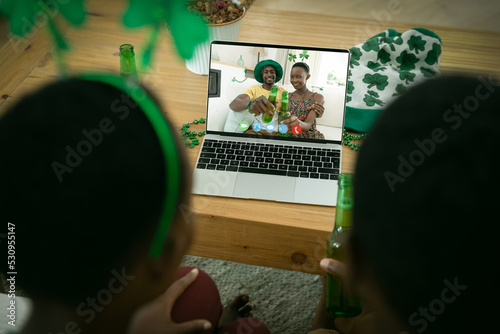 African american couple making st patrick's day video call with smiling couple on laptop at home
