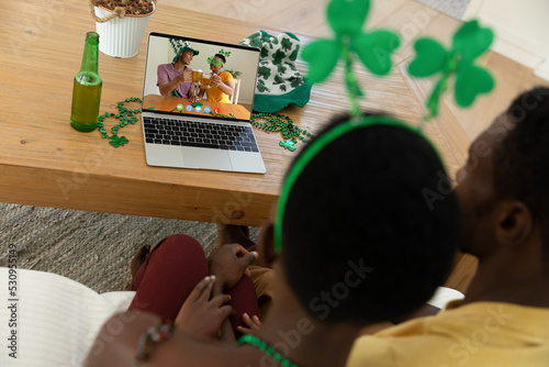 African american couple making st patrick's day video call with two male friends on laptop at home