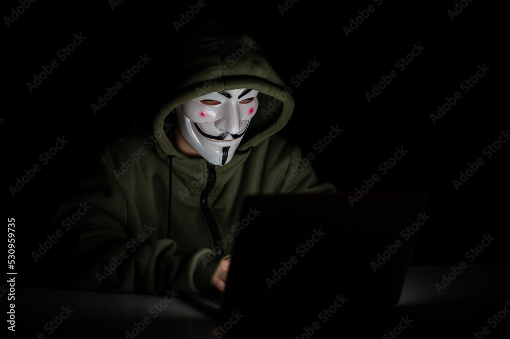 Anonymous in a hood is typing on a laptop in the dark. Anonymous in a hood is typing on a laptop in the dark.