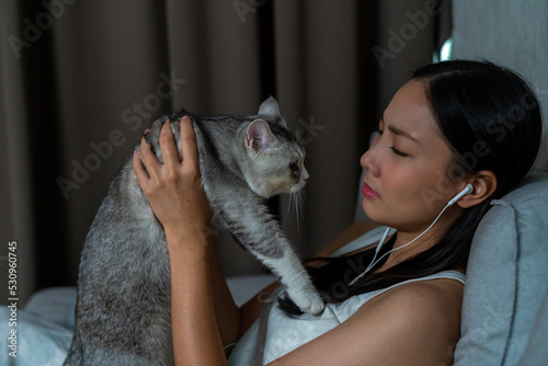 White tabby cat comforting his owner while she crying. Loneliness young Asian woman sitting on couch crying with sadness and negative emotion. Mental health  life problems and animal therapy concept.