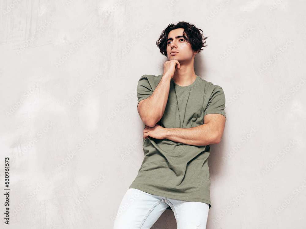Portrait of handsome confident stylish hipster lambersexual model.Man dressed in over size T-shirt and jeans. Fashion male isolated in studio. Posing near blue wall Portrait of handsome confident stylish hipster lambersexual model.Man dressed in over size T-shirt and jeans. Fashion male isolated in studio. Posing near blue wall