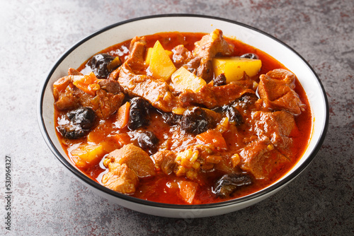 Khoresht Aloo Stewed lamb meat with dried plums or prunes, tomato, onion, potato, carrot and garlic closeup in the bowl on the table. Horizontal photo