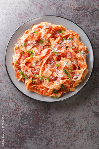 Pappardelle alla Fiesolana is a creamy and delicious dish made with pasta, bacon, onion, tomato and cheese closeup in the plate on the table. Vertical top view from above