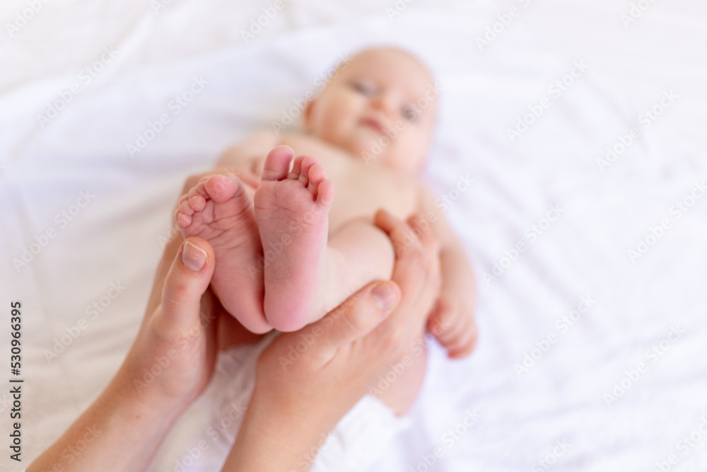 mom's hands hold the baby's legs in the crib on a white cotton bed, hygiene and care and care of the newborn mom's hands hold the baby's legs in the crib on a white cotton bed, hygiene and care and care of the newborn